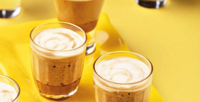 Fotografia em tons de amarelo em uma bancada de madeira amarela, um recipiente amarelo retangular e três copinhos de vidro com a mousse de café e caramelo dentro deles.