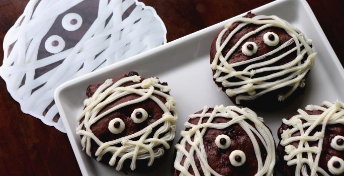Fotografia de cookies de chocolates cobertos por fios de chocolate branco para imitar uma múmia.