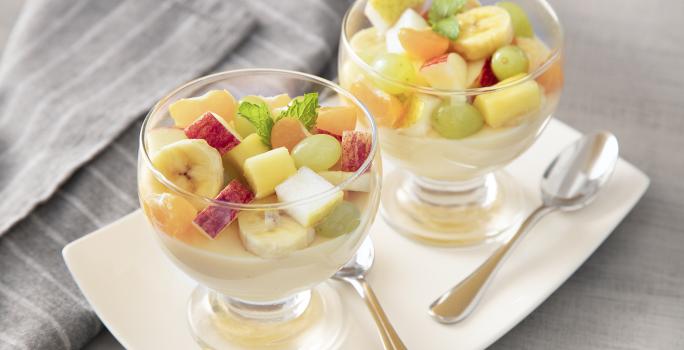 Receita de Gelatina de Frutas. Observa-se duas taças de vidro individuais sobre uma tábua branca e com gelatinas e frutas cortadas dentro.