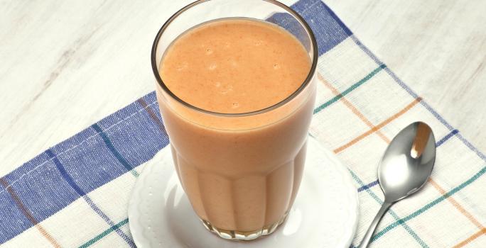 acima de um pano listrado nas cores azul e branco, contém um pratinho com o copo da vitamina e ao lado uma colher.