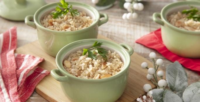 Foto da receita de arroz integral com amêndoas servida em três panelinhas verdes sobre uma tábua de madeira em cima de uma mesa decorada com elementos de inverno