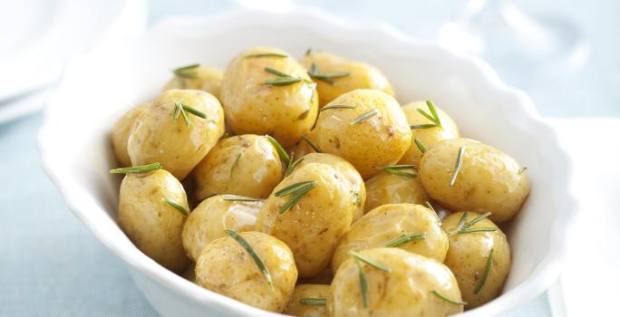 fotografia em tons de branca e azul de uma bancada vista de cima, contém um recipiente redondo e branco com bolinhas de batatas e alecrim por cima