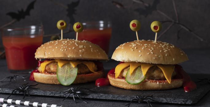 Fotografia de um hamburguer com carinha de "monstro", mostrando as camadas de frango empanado, pepino, queijo.