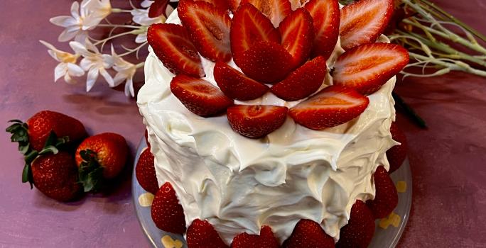 Receita de Bolo Confeitado com Chantininho. Observa-se um bolo alto coberto com chantinho e decorado com morangos.