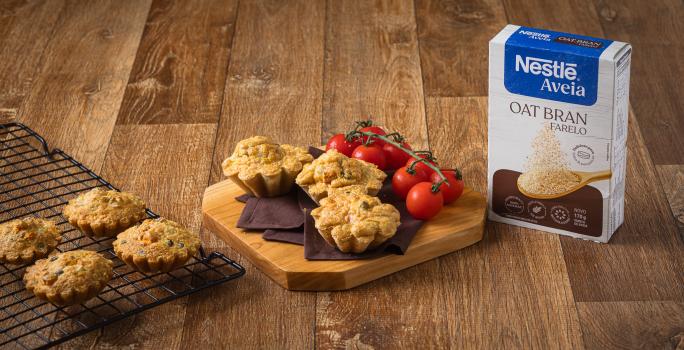 Foto da receita de tortinha de legumes com Nestlé Aveia disposta em 3 porções sobre uma tábua de madeira com tomates-cereja e a embalagem de aveia ao lado