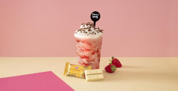 Foto em tons de cor de rosa da receita de smoothie de morango servida sobre uma mesa amarela com kit kat amarelo à frente