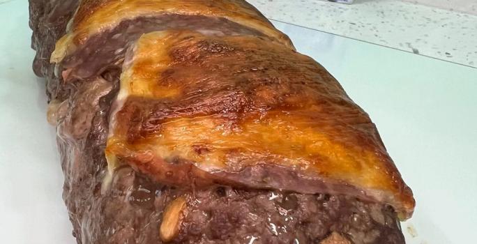 Foto da receita de rocambole de carne moída servida em uma porção grande sobre uma mesa branca