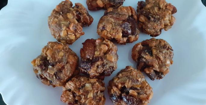 Foto em tons de marrom da receita de cookies de frutas secas e mucilon servida em diversas porções sobre um prato de porcelana branco