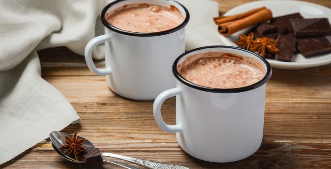 fotografia em tons de branco e marrom tirada de duas xicaras brancas com chocolate quente dentro