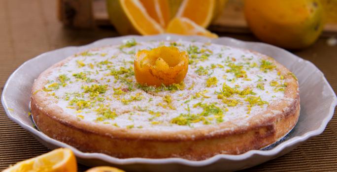 Foto aproximada da receita de bolo de casca de laranja, servido em um prato e decorado com açúcar e raspas de laranja.