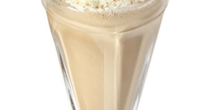 Fotografia vista de frente em tons de branco e marrom, ao centro um copo transparente com milkshake de café dentro e creme e canela por cima para decorar.
