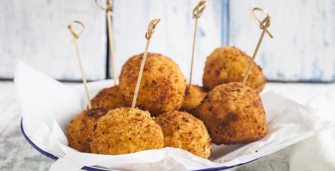 fotografia em tons de branco e bege de uma bancada cinza vista de frente. Contém um prato redondo branco com bolinhos de arroz frito, e por cima palitos.