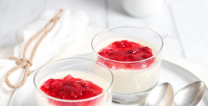 fotografia em tons de branco e vermelho tirada de um recipiente redondo branco, contém duas taças com mousse e calda de frutas vermelhas por cima