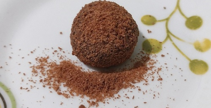 Foto da receita de Brigadeiro de Café. Observa-se um brigadeiro em um prato branco decorado com o café polvilhado por cima.