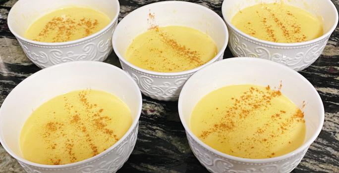 Foto de cinco potes brancos com a receita de curau cremoso em tom amarelo, polvilhado com canela em pó