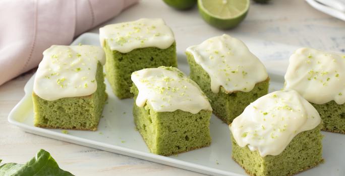 Foto de receita de Bolo de Couve com Calda de Limão. Observa-se uma tábua branca com 6 pedaços de bolo verde com calda de limão.