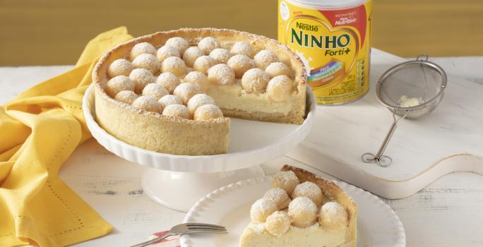 Fotografia em tons de branco e laranja de um prato redondo laranja com uma torta com recheio branco e brigadeiros brancos enrolados.