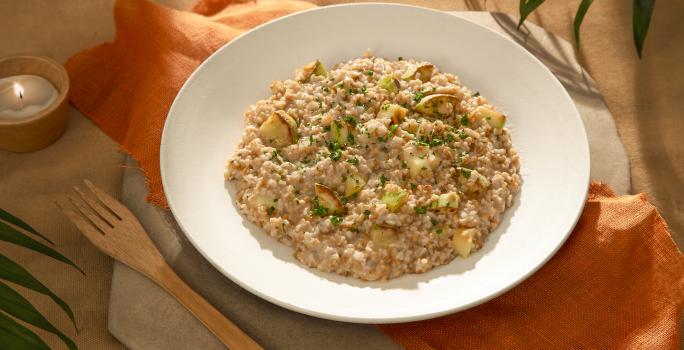 Foto da receita de risoto de abobrinha vegano servida em um prato de cerâmica com um garfo de madeira ao lado sobre um paninho laranja