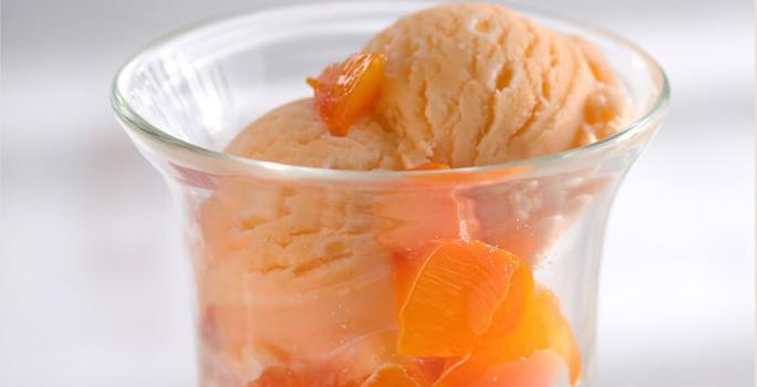 foto tirada de um copo transparente com bolas de sorvete de caqui e pedaços da fruta.
