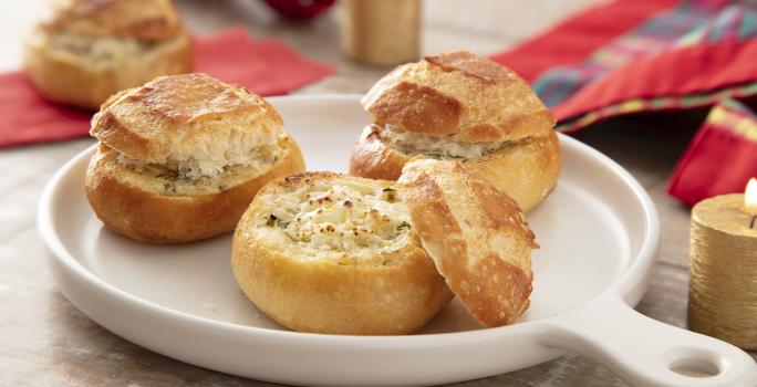 Foto da receita de Pão de Alho na Air Fryer. Observa-se três pãezinhos italianos em um recipiente refratário branco de porcelana, sendo que o da frente está aberto expondo o recheio de queijo.