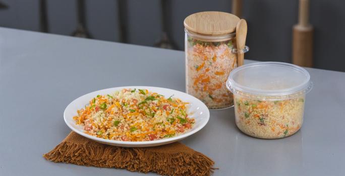 Foto da receita de salada de quinoa, servida em um prato branco, sobre uma tábua, e armazenada em potinhos de varios tamanhos