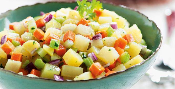 foto tirada de um suporte para servir pratos na cor verde e dentro contém a salada com pedaços de batata-doce, salsão, cenoura e cebola roxa.