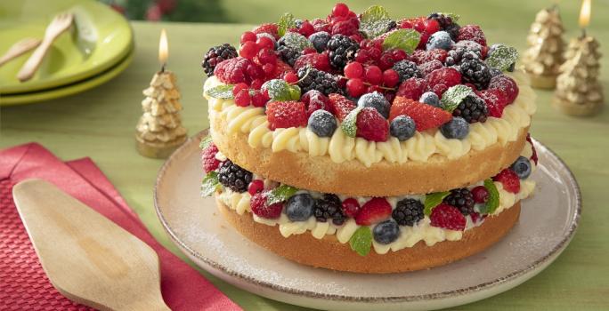 Foto da receita de bolo pelado naked cake natalino sem glúten servida sobre uma base bege em cima de uma mesa verde com decorações de natal, além de um pano vermelho com uma espátula de madeira em cima