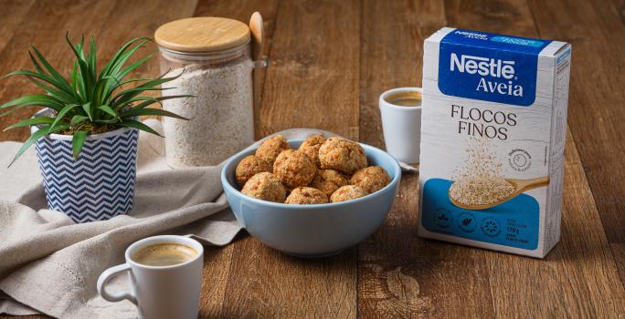 Foto da receita de bolinha crocante de queijo com nestlé aveia disposta em diversas porções dentro de um pote azul claro com um vaso de planta e a embalagem de aveia ao lado
