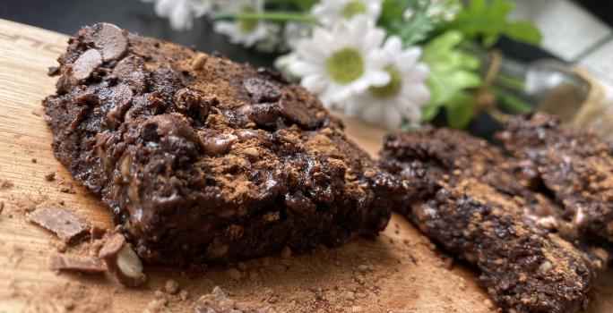 Imagem da receita de Brownie Rápido de Chocolate com Aveia sobre uma mesa e atrás umas flores