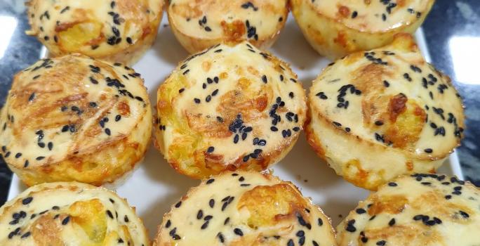 Foto da receita de Pão de Queijo Funcional. Observa-se um prato branco quadrado com 9 unidades de pão de queijo polvilhados de gergelim preto em cima.