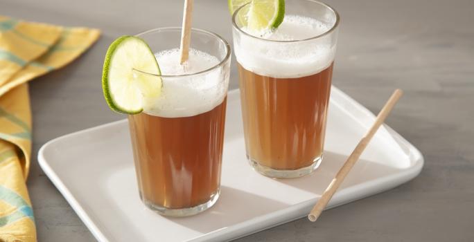 Foto da receita de Suco de Mate com Limão. Observa-se dois copos decorados com uma rodela de limão e com a bebida dentro