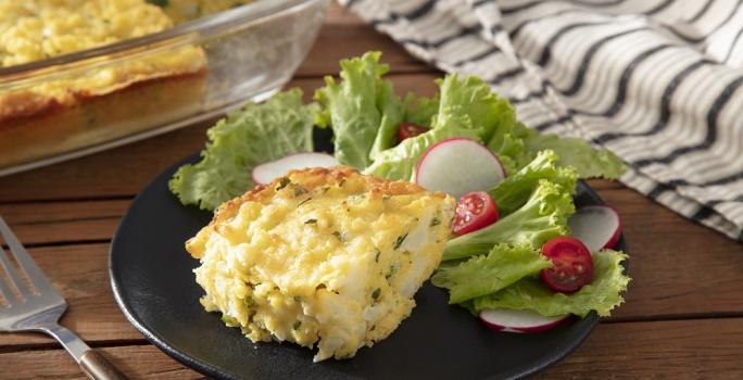 Foto da receita de bolo salgado servida com salada de alface em um prato de porcelana preto sobre uma mesa de madeira com uma espátula prateada ao lado