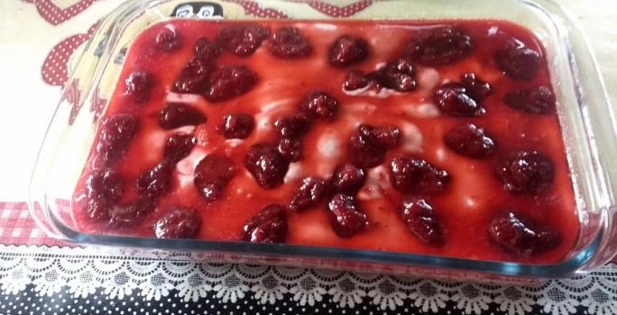 Foto em tons de vermelho da receita de mousse de frutas servida em um refratário de vidro grande com calda de frutas vermelhas por cima