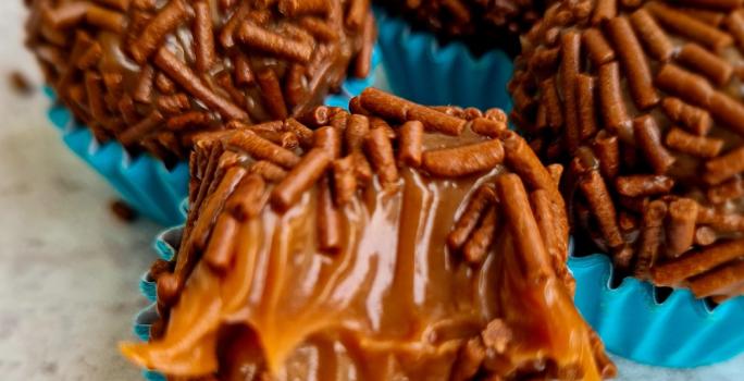 Foto da receita de Brigadeiro Maravilhoso. Observa-se quatro brigadeiros com granulado em forminhas azuis. O da frente está mordido para mostrar a cremosidade.