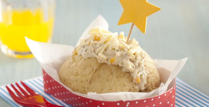 foto em tons de azul, branco e vermelho tirada de um pano listrado em tons de azul e branco. Contém um recipiente vermelho com bolinhas brancas com uma batata e creme de frango por cima e ao lado um garfo para servir