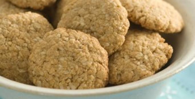 Fotografia em tons de azul, branco e pardo de uma bancada vista de frente, um pano azul e por cima um recipiente redondo e branco com biscoitos dentro.