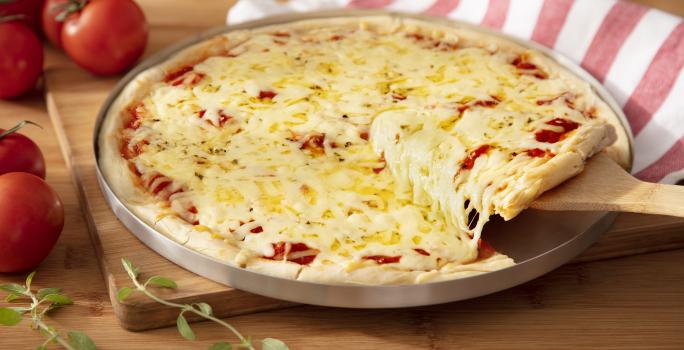 Fotografia em tons de vermelho em uma bancada de madeira clara, uma tábua de madeira, um pano branco com listras vermelhas, uma forma de pizza com a pizza de muçarela em cima dela e uma espátula de madeira tirando um pedaço. Ao lado, tomates para decorar. Fotografia em tons de vermelho em uma bancada de madeira clara, uma tábua de madeira, um pano branco com listras vermelhas, uma forma de pizza com a pizza de muçarela em cima dela e uma espátula de madeira tirando um pedaço. Ao lado, tomates para decorar.