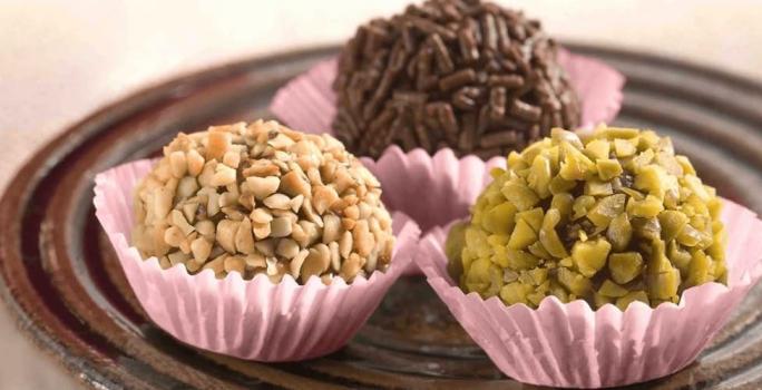 3 brigadeiros em forminhas lilás um com granulado por cima e os outros com castanhas picadas