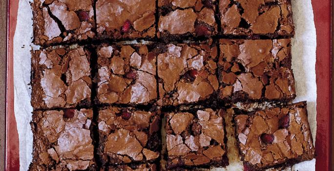 fotografia em tons de marrom e branco de uma bancada vista de cima, contém um pano branco e por cima pedaços quadrados de bolo de chocolate