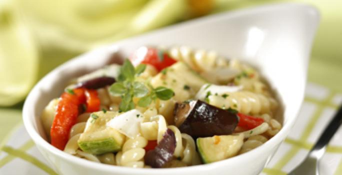 Fotografia em tons de verde em uma mesa de madeira verde com um guardanapo de papel quadriculado em branco e verde e um potinho branco com a salada mediterrânea dentro.