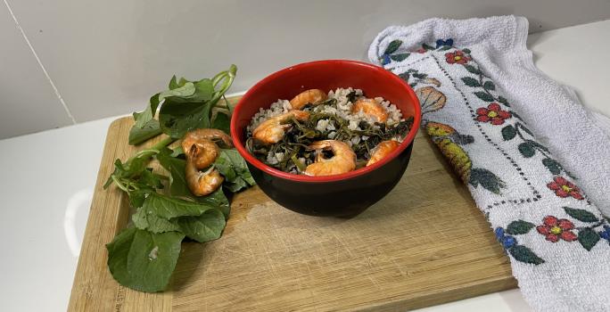 Imagem da receita de Arroz Paraense Nutritivo em um recipiente, sobre uma tábua, e ao lado folhas der jambu e camarão