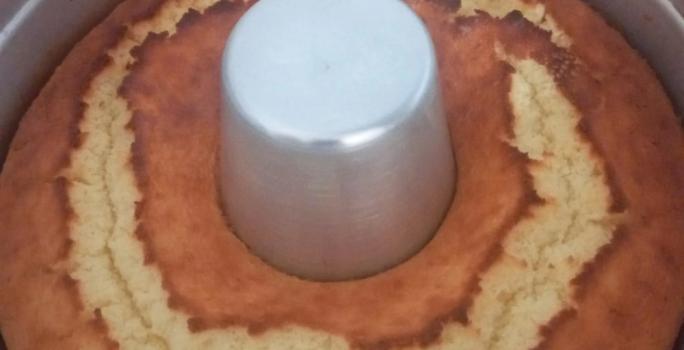 Foto da receita de Bolo de Arroz Cru. Observa-se um bolo assado ainda dentro de uma forma com furo no meio