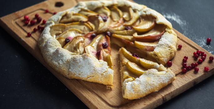 Fotografia em tons de marrom com uma tábua de madeira ao centro. Em cima da tábua existe uma torta rústica de maçã com a massa feita de NESTLÉ Farinha de aveia.