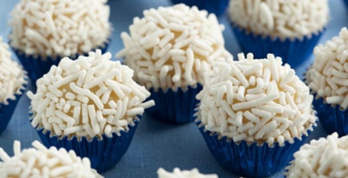 Fotografia em tons de branco e azul de vários brigadeiros em forminhas azuis metalizadas com granulado branco.