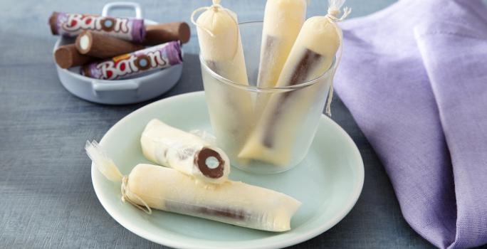 Foto da receita de geladinho algodão doce servida em 5 porções dentro de um pote transparente em cima de um prato de porcelana com um paninho lilás e algumas unidades de baton ao fundo