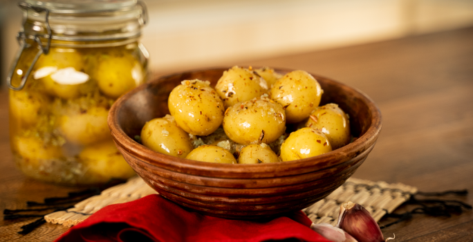 Foto da receita de Batata Bolinha em Conserva. Na foto, observa-se as batatas em um recipiente redondo e, a fundo, um pote hermético transparente com as batatas na conserva.