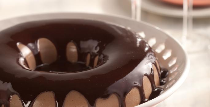 em um recipiente branco e redondo contém uma cassata de chocolate com cobertura de chocolate por cima.