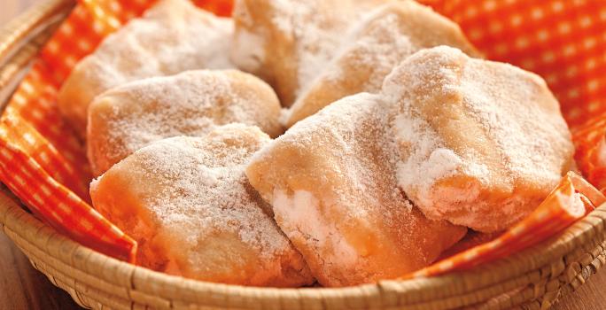 Fotografia em tons de laranja em uma bancada de madeira escura com uma cesta de vime com guardanapo laranja de bolinhas com algumas palhas italianas feitas com tangerina dentro dela.