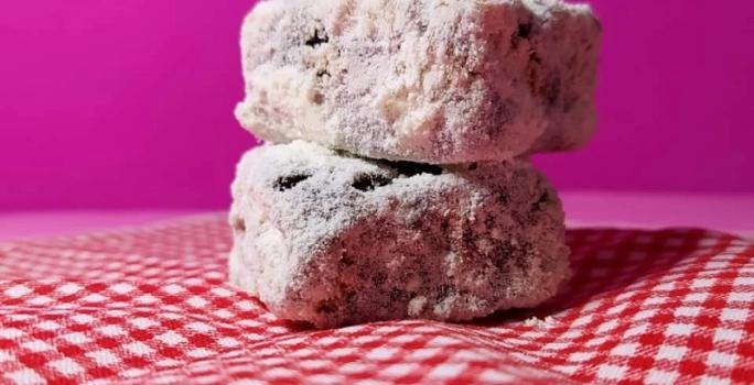 Foto da receita de Palha Italiana. Observa-se duas palhas italianas cortadas em quadrados dispostas em uma toalha quadriculada branca e vermelha e em um fundo rosa.