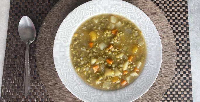 Imagem da receita de Sopa de Ervilha com Legumes, em um prato branco, sobre uma mesa e ao lado uma colher